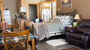Una habitación acogedora con cama, sofá, mesa de comedor con sillas, zona de cocina y ventilador de techo.
