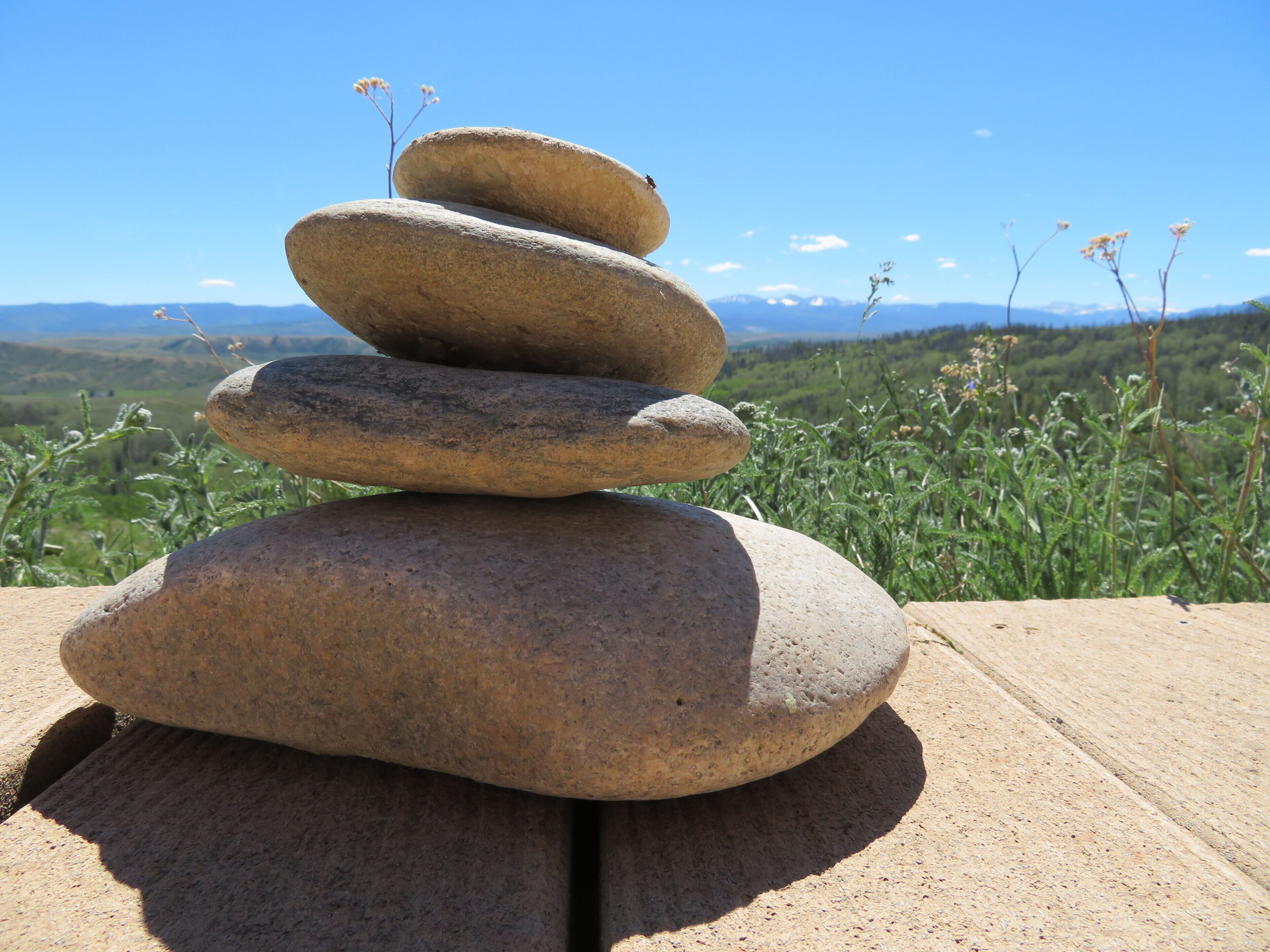 A stack of smooth, rounded stones on a wooden surface with a clear view of a mountainous landscape in the background.