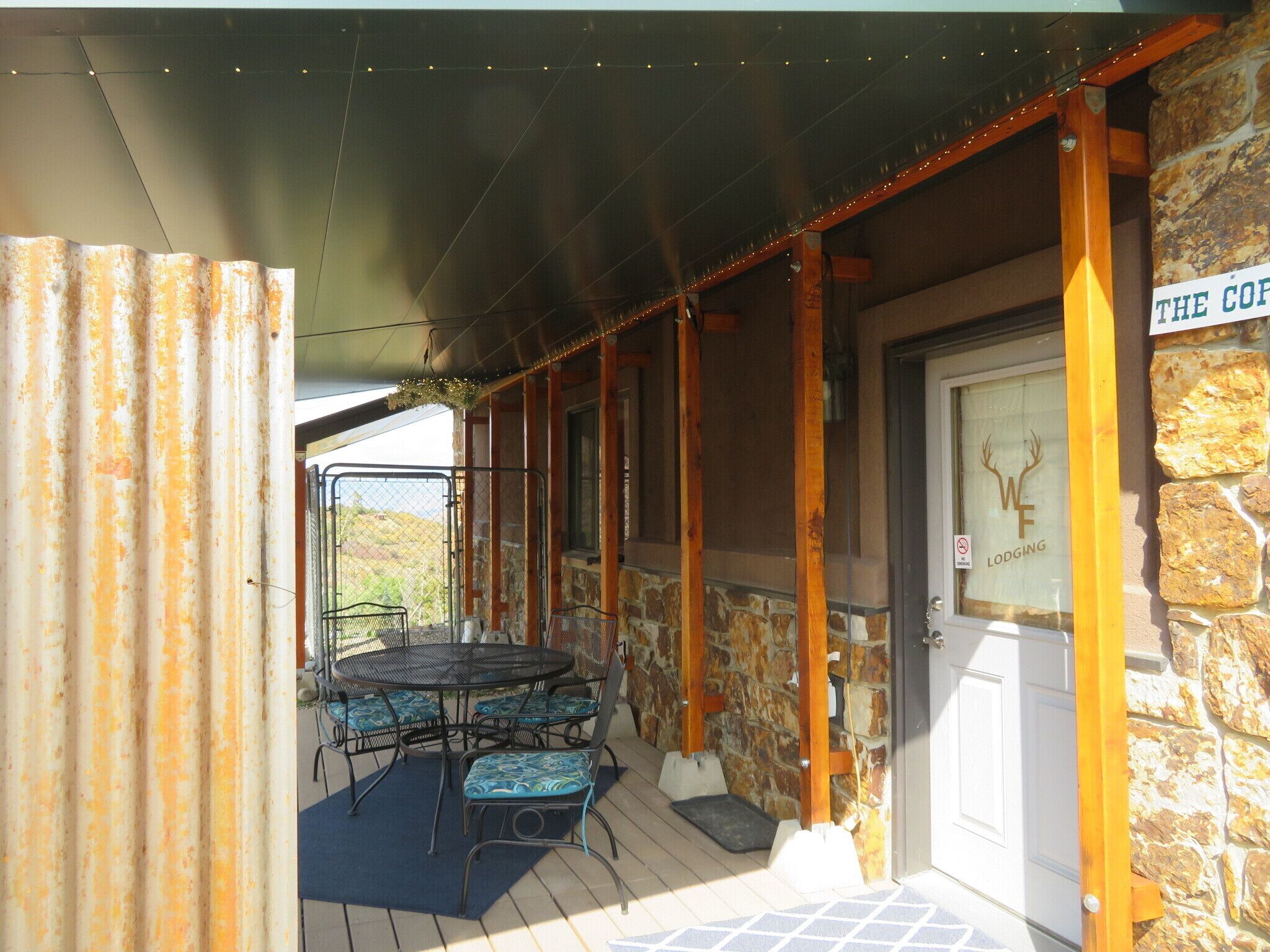 A covered patio area with a table and chairs, a stone wall, and a door with a sign.