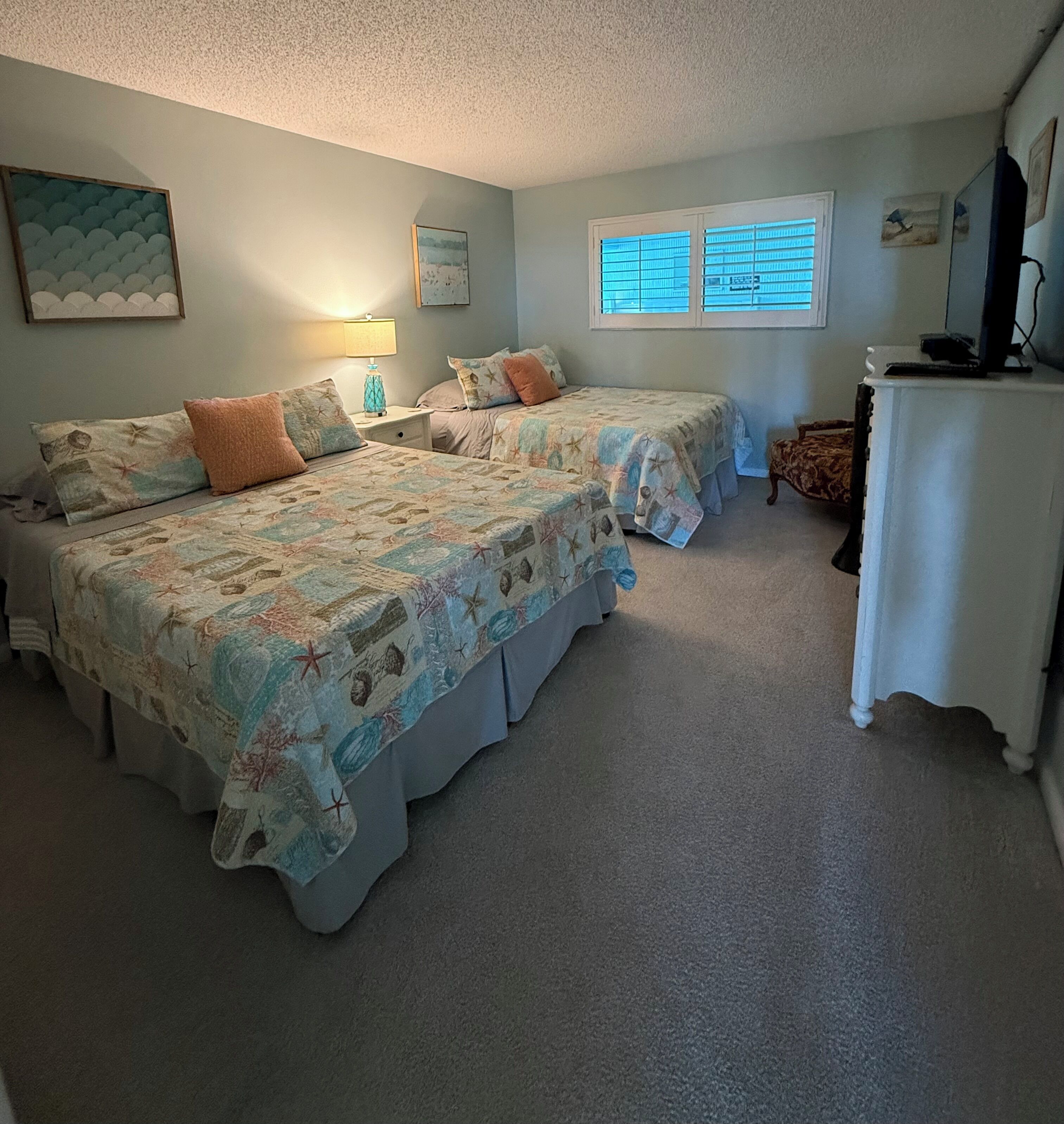 A bedroom with two beds, a desk, and a window with blinds.