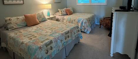 A bedroom with two beds, a desk, and a window with blinds.