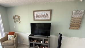 A living room with a television, a coffee table with a remote control, and a bookshelf with decorative items. - Cocoa Beach Paradise - direct ocean (Cocoa Beach)