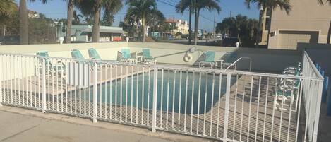 A swimming pool with a white fence, green lounge chairs, and palm trees in the background.