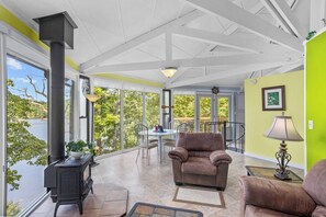 A sunroom with a fireplace, a dining table, and a view of a lake.