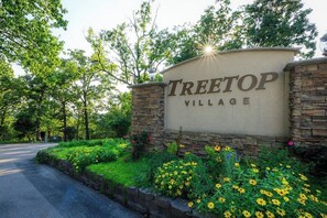 Een bordje voor Treetop Village met een stenen muur en groen.