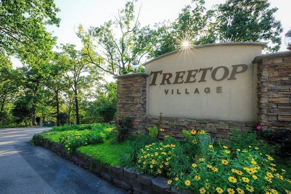 Señal de Treetop Village con un muro de piedra y follaje.