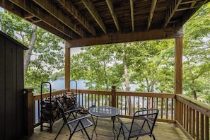 A wooden deck with a table and chairs, overlooking a body of water and trees.