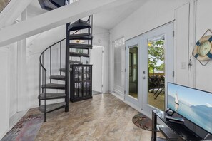 A spiral staircase, a sliding glass door, and a television in a room with tiled flooring.