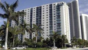 A multi-story hotel with a modern design, featuring a central courtyard with palm trees and a parking area in front. - Breathtaking 2/2 Ocean View Fully Remodeled Condo! (Hollywood)