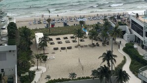 A beach with umbrellas and lounge chairs, a sandy area with palm trees, and a view of the ocean. - Breathtaking 2/2 Ocean View Fully Remodeled Condo! (Hollywood)
