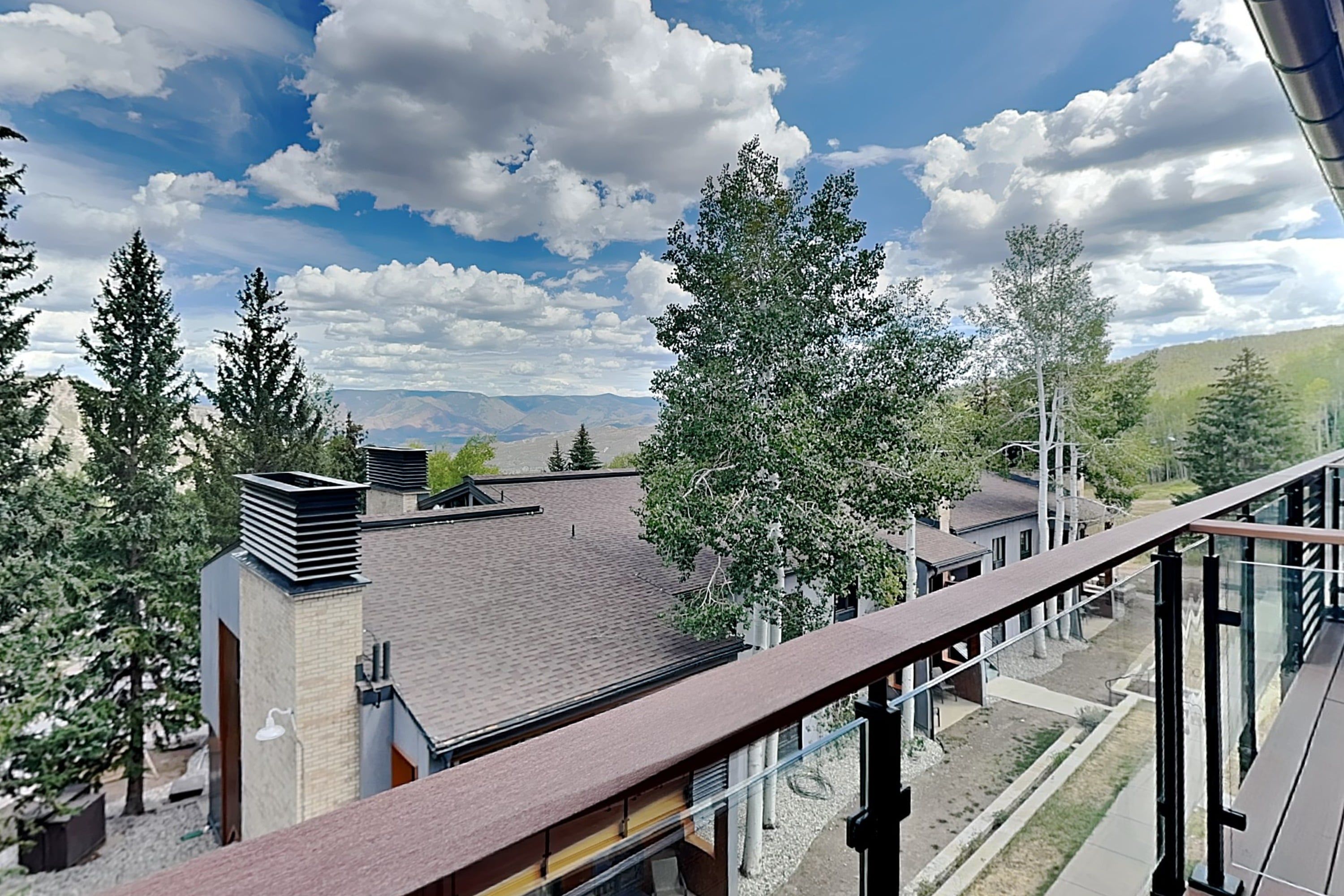 Un balcon offrant une vue sur un paysage montagneux, des bâtiments modernes et de grands arbres.