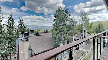 Un balcón con vistas a un paisaje montañoso, edificios modernos y altos árboles.