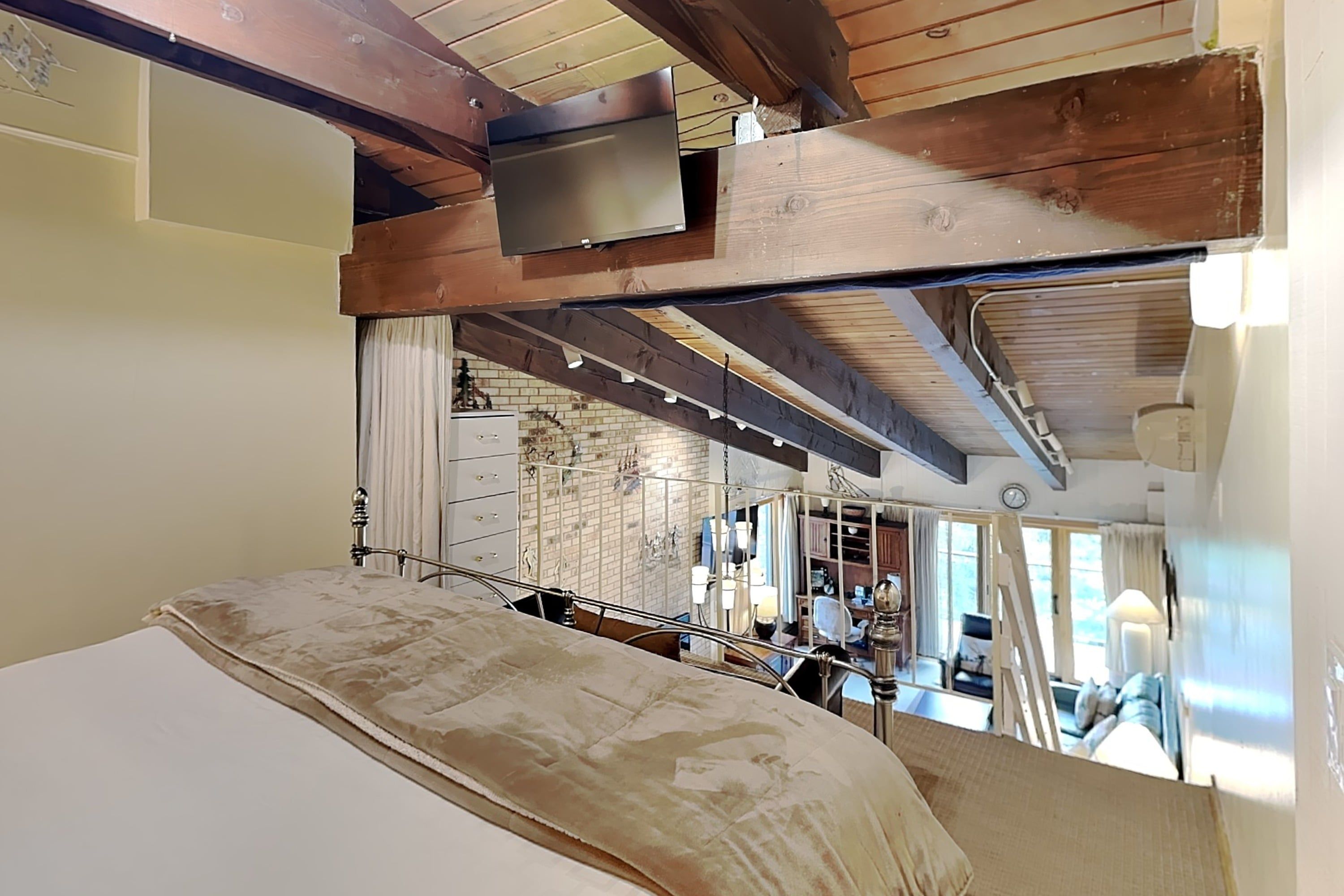 Une pièce avec un lit, un téléviseur fixé au plafond et un mur de briques avec une fenêtre.
