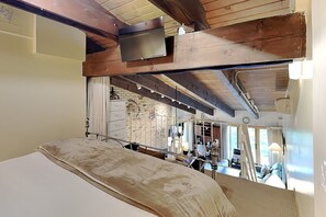 A room with a bed, a television mounted on the ceiling, and a brick wall with a window. - 🌲Timberline 301 Studio Loft Standard ~ Hot Tub~Pool~WiFi~Ski-in/out~Local Shuttle🌲 (Snowmass Village)