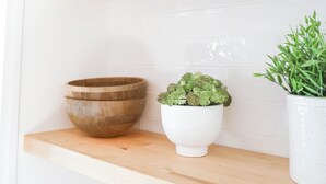 Ein Küchenregal mit einer Holzkugel, einem weißen Topf mit einer Pflanze und einem gewebten Korb.