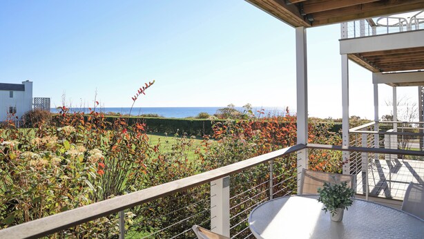 Ein Balkon mit Meerblick, ein Tisch mit einem Blumentopf und eine Holzbalkendecke.