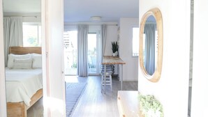 Ein Schlafzimmer mit Bett, ein Badezimmer mit Spiegel und eine Küchenzeile mit Tisch und Hocker.