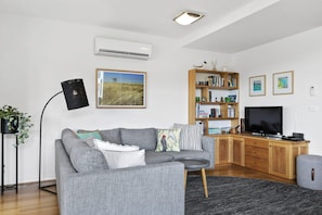 A modern living room with a grey sofa, a wooden bookshelf, a flat-screen TV, and a black floor lamp. - Point Grey Apartment One (Lorne)