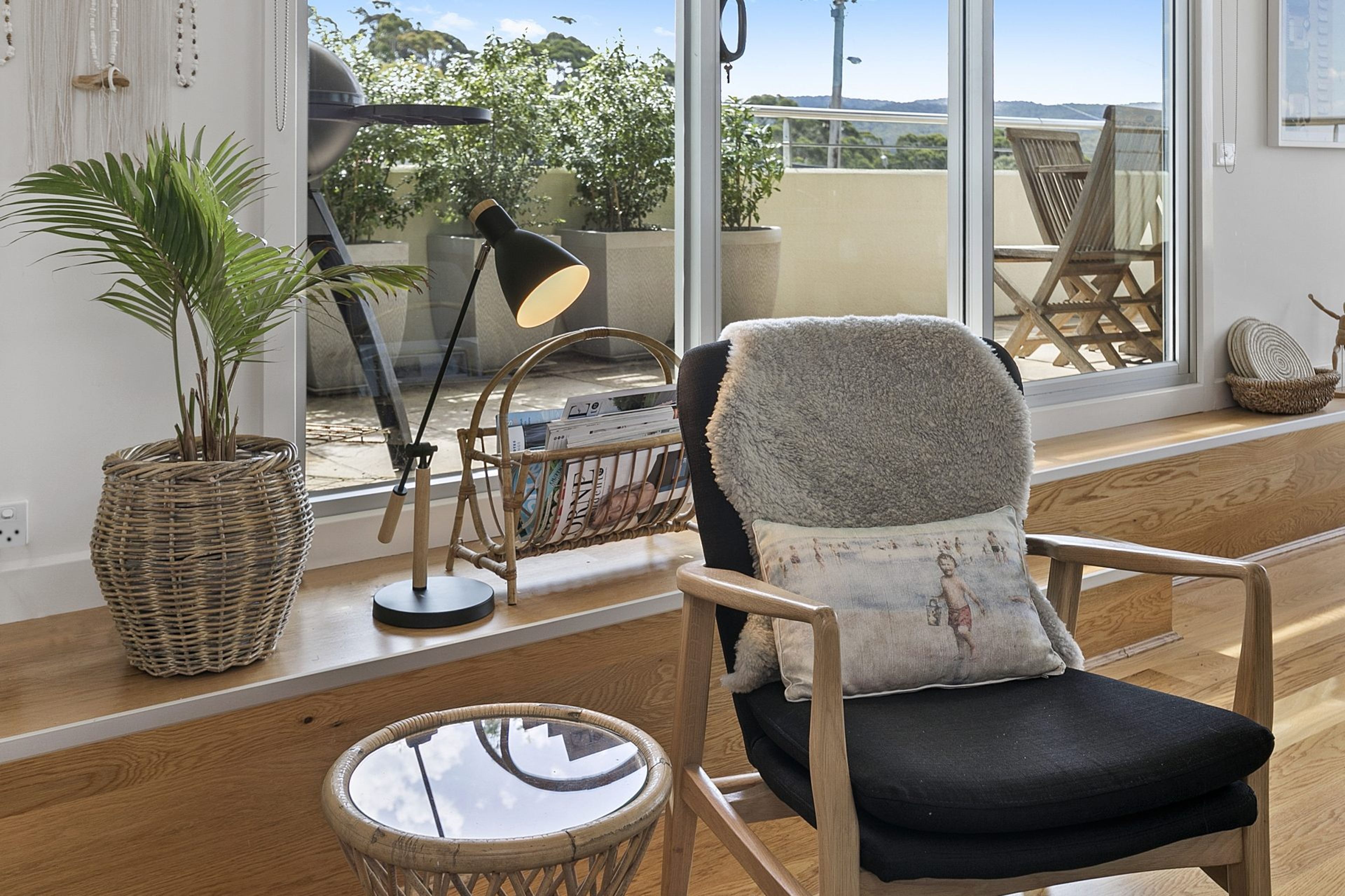 Une pièce avec une grande fenêtre, un fauteuil doté d'un coussin moelleux, une lampe, un panier en osier et une petite table ronde.