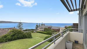A balcony with a view of the sea and a grassy area with trees.