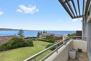 A balcony with a view of the sea and a grassy area with trees.