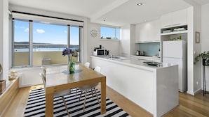 A modern kitchen with a central island, white cabinetry, and a view of the sea through large windows.