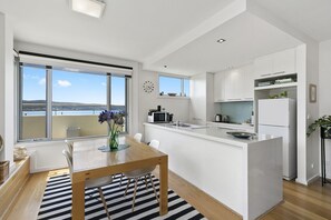 A modern kitchen with a central island, white cabinetry, and a view of the sea through large windows.