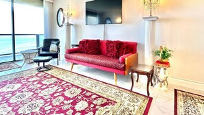 Un salon moderne avec un canapé rouge, un fauteuil noir, une grande moquette et une vue sur l’océan.