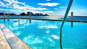 Une piscine à l’eau d’un bleu cristallin, avec vue sur l’eau et, en arrière-plan, le panorama de la ville.