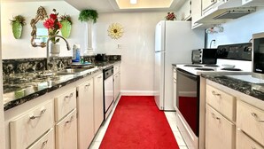 Une cuisine dotée de plans de travail en granit, d’une moquette rouge, d’un réfrigérateur, d’une cuisinière et d’armoires.