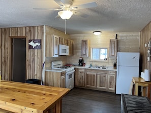 Kitchen features a central island, microwave, gas stove, refrigerator, and sink under a window.