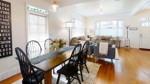 A spacious living room with a wooden dining table, black chairs, a grey sofa, and a blue armchair. There is a large window providing natural light and a view of the outdoors. - Beautiful Magnolia House in Napa Valley! (Napa)