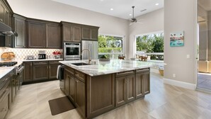 A spacious kitchen with dark wood cabinets, a large island, stainless steel appliances, and a view of the outdoors. - 3 Bedroom, PGA West home, Private Pool & Spa, #063306 (La Quinta)