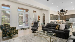 A spacious living room with a black leather sofa, a glass coffee table, and a patterned armchair. - 3 Bedroom, PGA West home, Private Pool & Spa, #063306 (La Quinta)