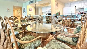Een eetgedeelte met een ronde glazen tafel, omringd door rieten stoelen met gestreepte kussens.