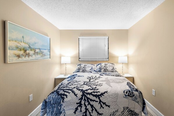 A bedroom with a bed, two bedside lamps, a painting on the wall, and a window with blinds.