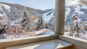 Vista desde una ventana que da a un paisaje nevado con árboles y un edificio a lo lejos.