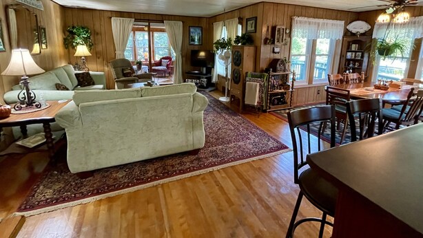 Un salon confortable avec un canapé, une table à manger et des chaises. Il y a des fenêtres avec des rideaux, un téléviseur et un ventilateur de plafond.