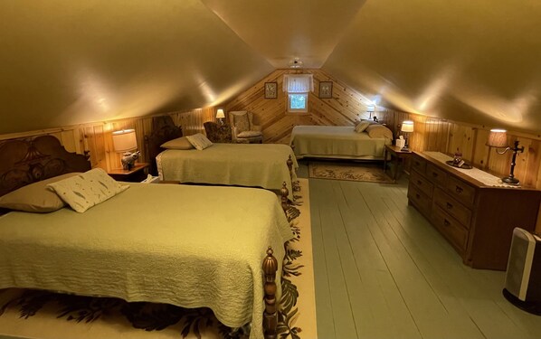 Une chambre mansardée chaleureuse, avec deux lits, une commode et une petite fenêtre.