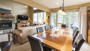 Un coin repas comprenant une table en bois, des chaises, un canapé, un téléviseur et une cheminée.