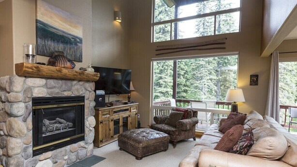 Un salon chaleureux avec une cheminée en pierre, des fauteuils confortables et de grandes fenêtres donnant sur l’extérieur.