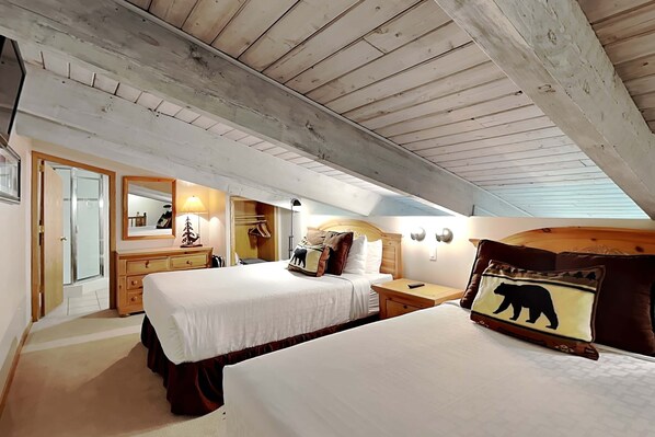 Une chambre avec un plafond en bois, un lit avec une literie blanche, une table de chevet, une commode, un miroir et une lampe.