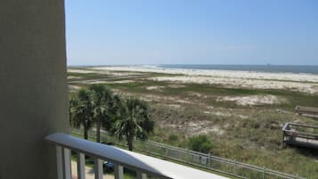 A balcony with a view of a beach, palm trees, and a swimming pool.