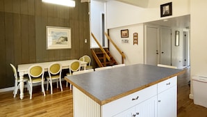 A kitchen with a dining area, wooden flooring, a ceiling fan, and a staircase leading to another room. - McNeal Cottage:  Comfortable home, large private back yard. (Ocracoke)