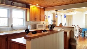 A kitchen with wooden cabinets, a central island, a microwave, and pendant lights. - The Mary Francis: Dog friendly, near Springers Point and Lighthouse (Ocracoke)