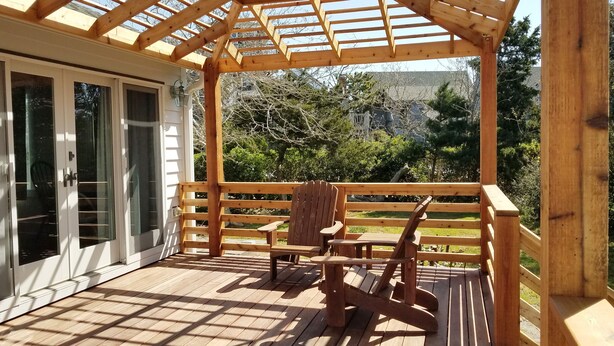 A wooden deck with a pergola, a rocking chair, and a table. - The Mary Francis: Dog friendly, near Springers Point and Lighthouse (Ocracoke)