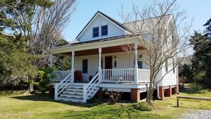 A two-story house with a porch, a small staircase, and a brick foundation. - The Mary Francis: Dog friendly, near Springers Point and Lighthouse (Ocracoke)