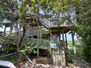 Une structure en bois à plusieurs niveaux, dotée d’un escalier et entourée d’un feuillage dense.