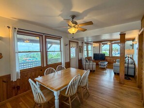 A dining area with a wooden table and white chairs, a television, and a ceiling fan.