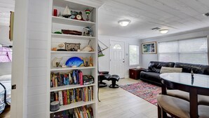 A living room with a bookshelf, a black leather sofa, a dining table, and a colorful rug.